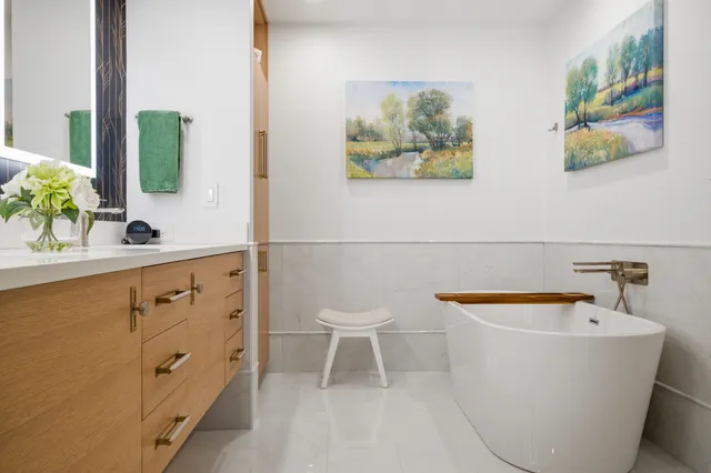 Oak floating vanity and freestanding tub in a Braintree primary bath finished with white quartz and marble-look wall tile.