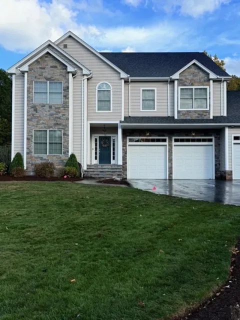 Two-story suburban house with brick and vinyl siding exterior, stone accents, front lawn, and attached double garage.