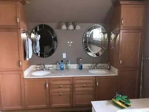 Bathroom vanity with double sinks, two round mirrors, and wood cabinets under warm lighting