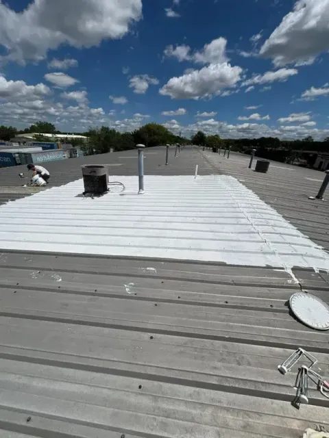 Rooftop with white coating, vents, and blue sky with scattered clouds.