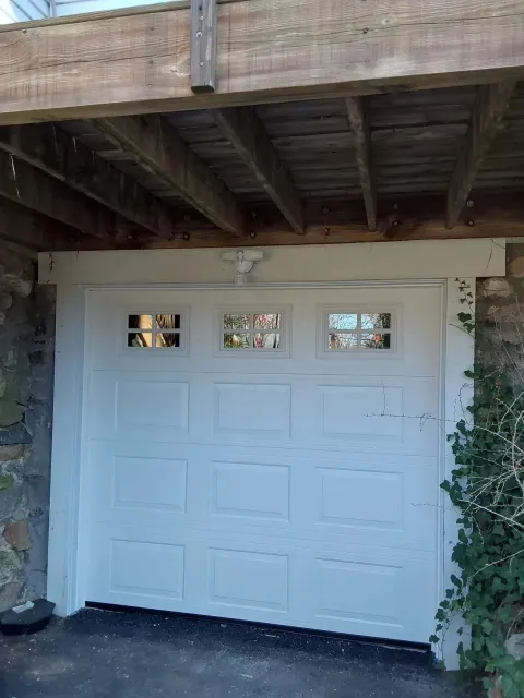 White garage door beneath a wooden deck, framed by stone walls and ivy.