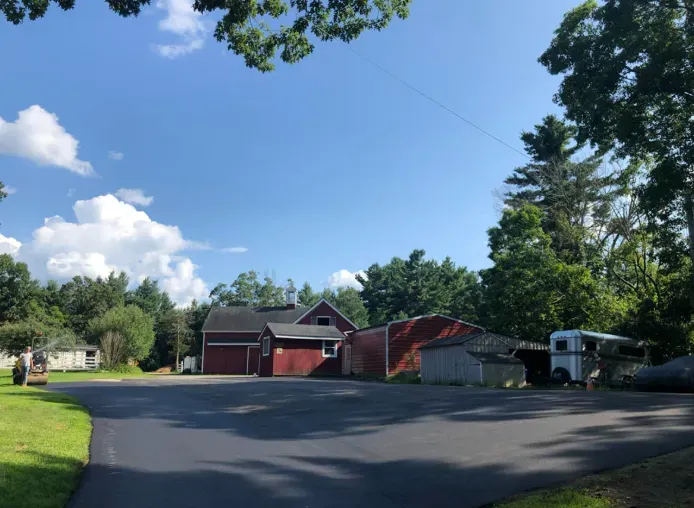 Quiet residential driveway with red garage buildings, parked vehicles, and trees under a blue sky