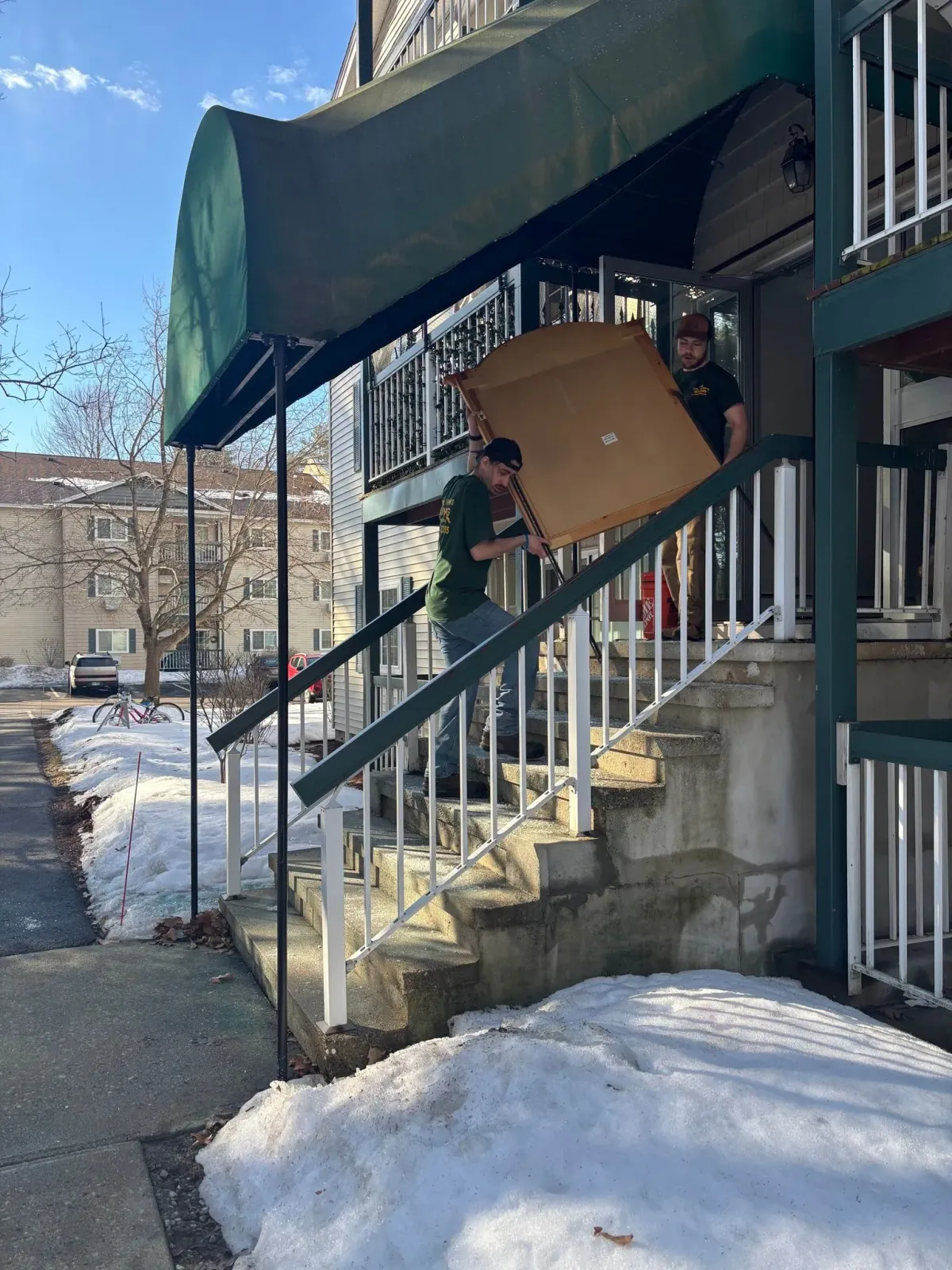 Snowy apartment entrance with stairs, green awning, and a large cardboard box propped on the landing
