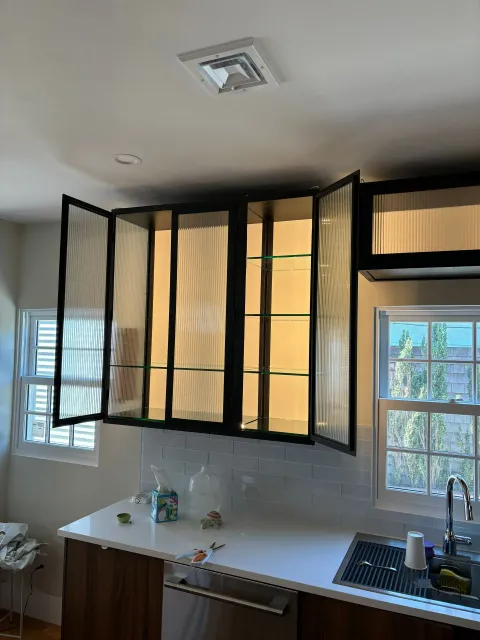 Modern kitchen cabinets with black frames, rippled glass doors, and interior lighting above a countertop.