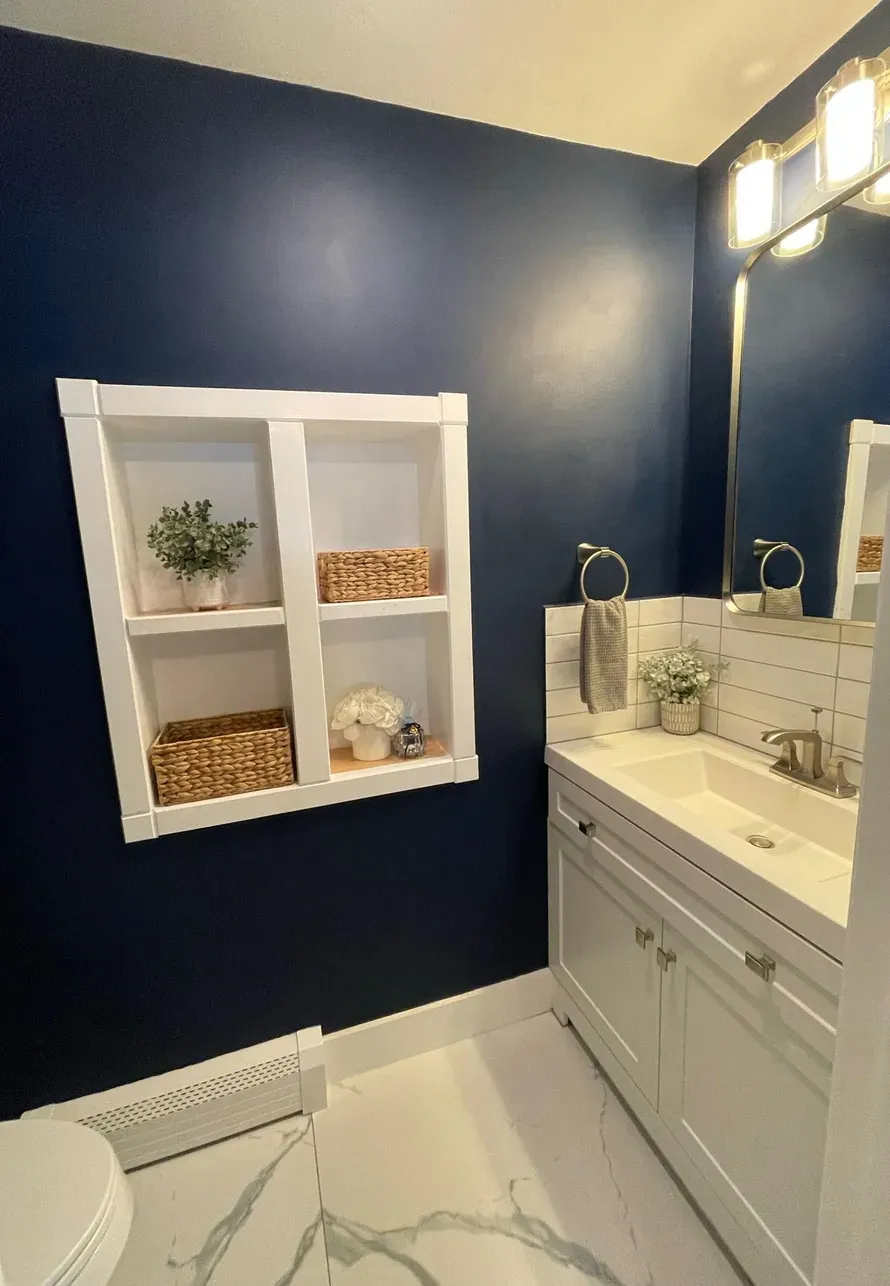 A bathroom featuring dark blue walls, a white built-in shelving unit, a white vanity with a sink, and a light-colored floor.