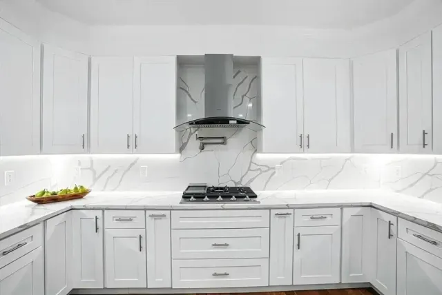 White kitchen with marble countertops, cabinets, and range hood.