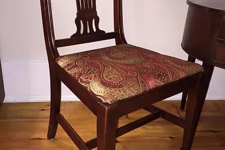 A refinished antique chair. Dark wood with a richly designed panel cushion.