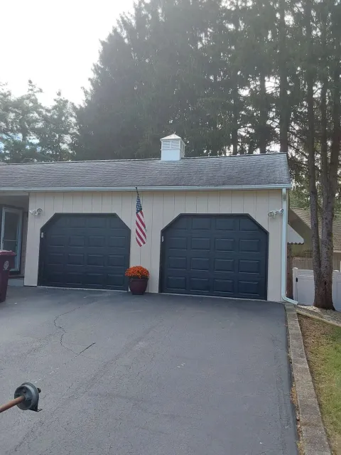 Two-car garage with dark blue doors, American flag, and flower pot in front of a beige house