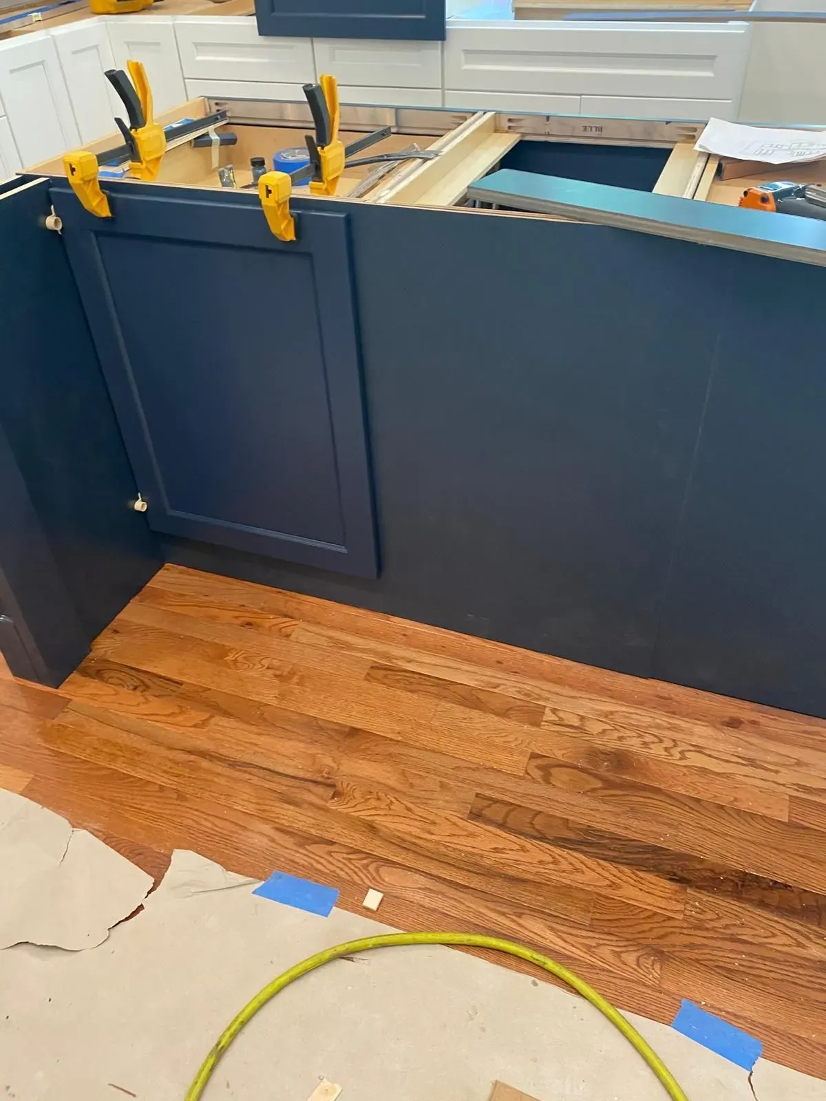 Blue kitchen island with wood floor and yellow clamps, suggesting cabinet installation or repair