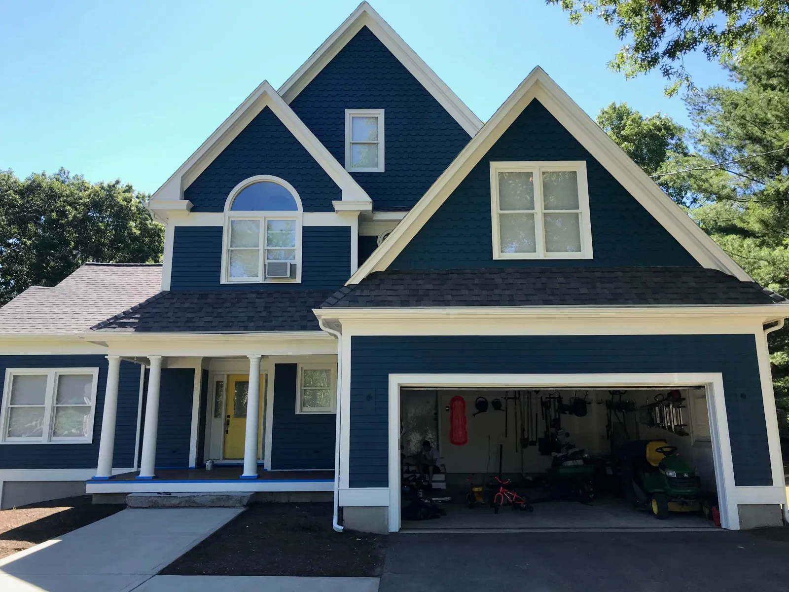 Blue two-story house with a yellow front door and white trim. The garage is open, displaying tools and lawn equipment.