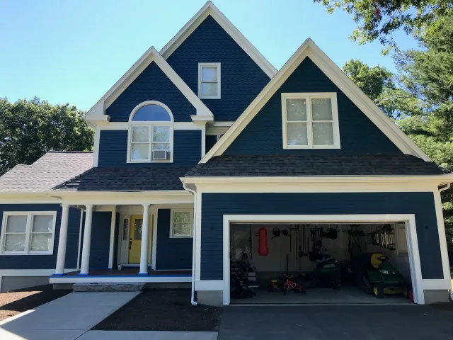 Blue two-story house with a yellow front door and white trim. The garage is open, displaying tools and lawn equipment.