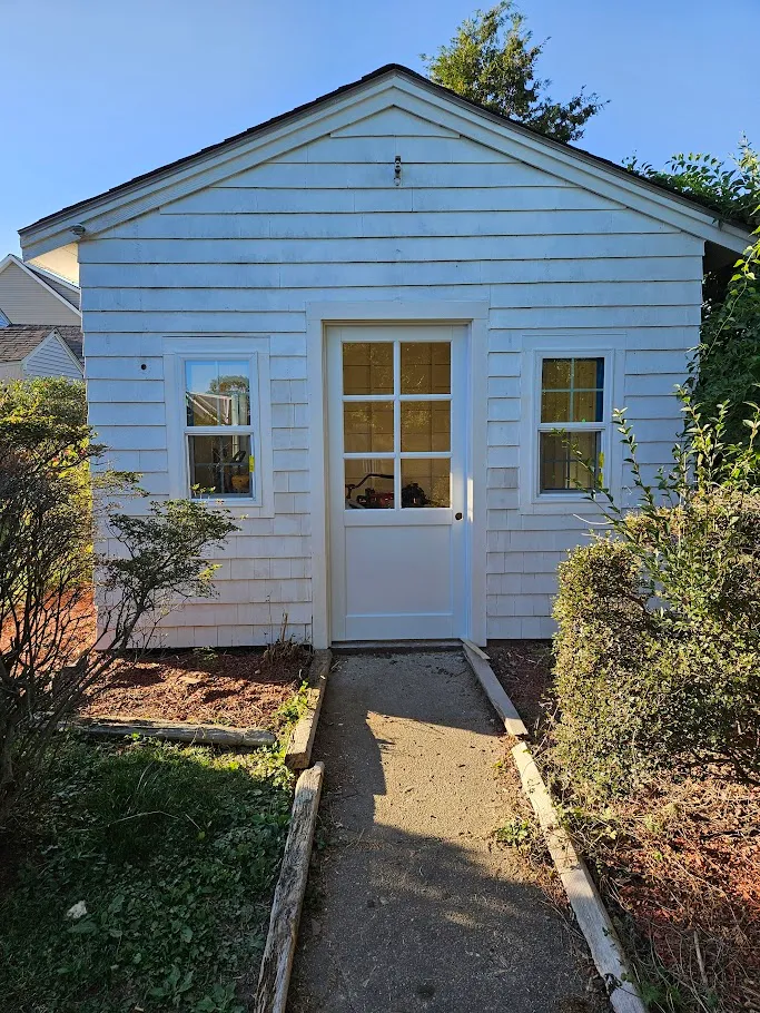 Backyard shed converted into a white studio with a new six-lite door and replacement windows in Middletown, Rhode Island by Toensing Construction