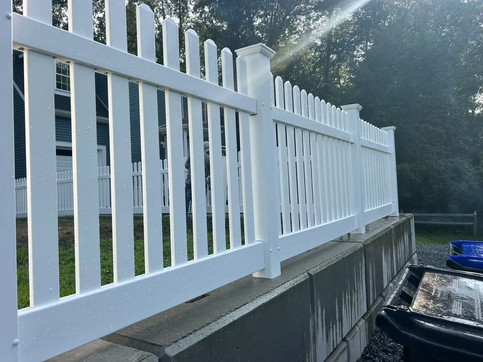 White vinyl fence along a concrete retaining wall beside a driveway in bright daylight