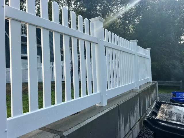 White vinyl fence along a concrete retaining wall beside a driveway in bright daylight