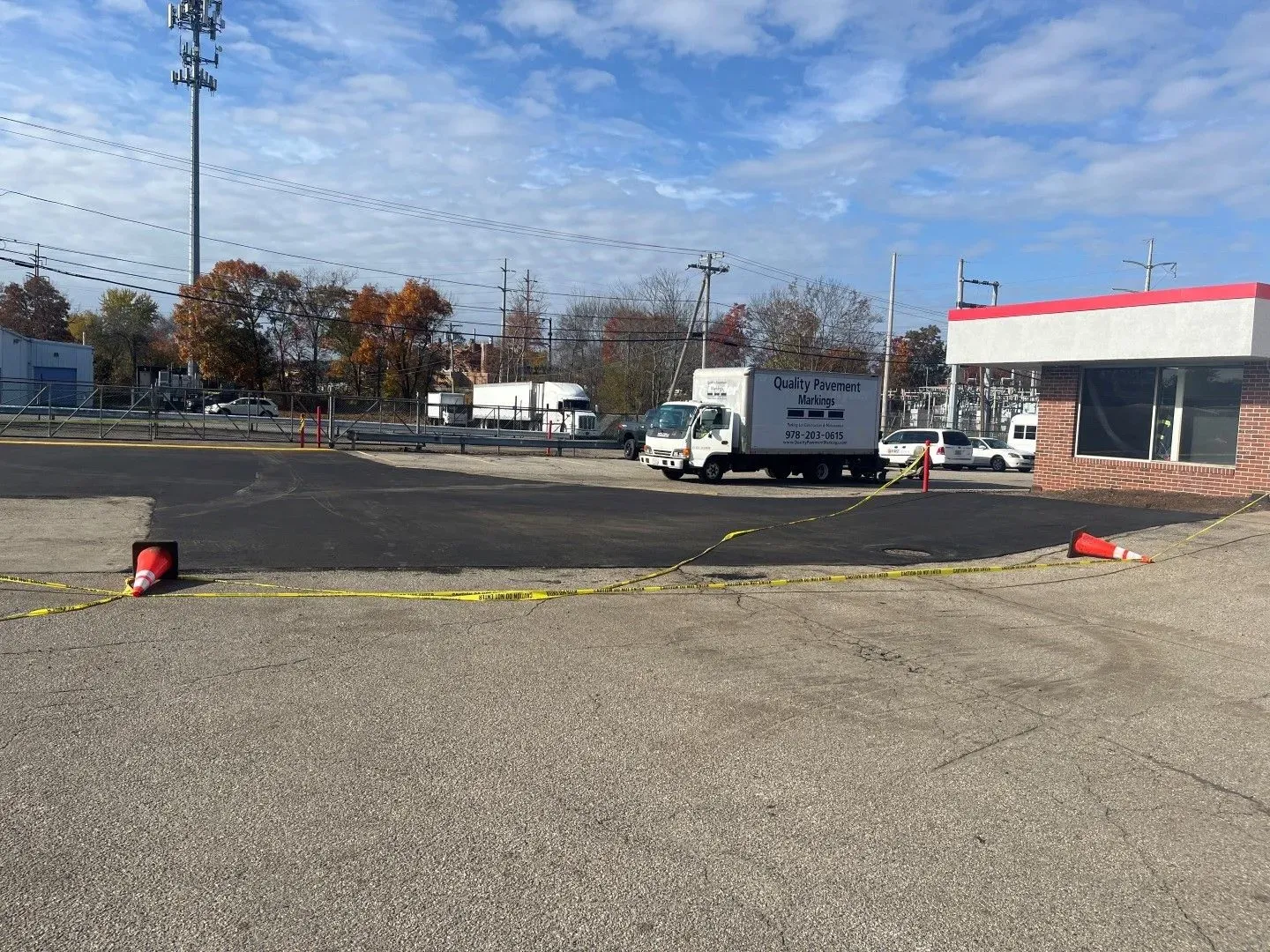 Empty parking lot beside a red-trimmed building with a white truck under a cloudy sky