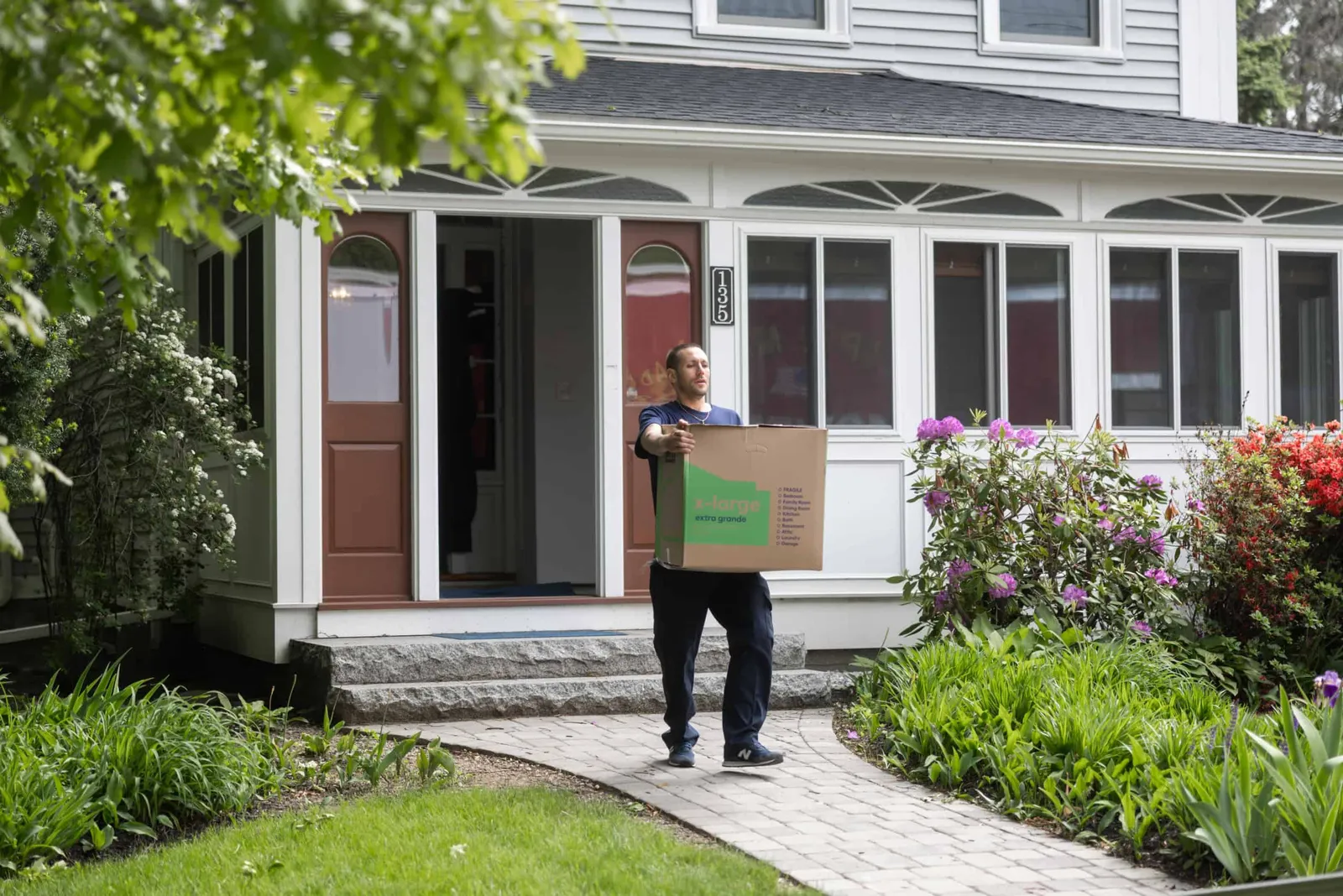 A man holding a moving box outside of a house.