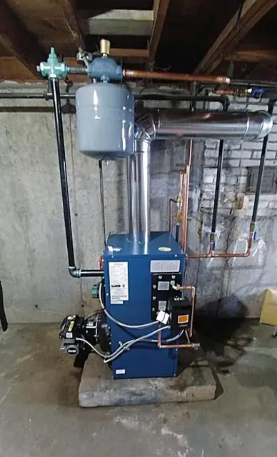A blue boiler is sitting in a basement next to a brick wall.