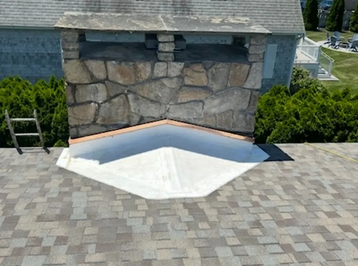 Stone retaining wall with a white concrete ramp in front of a house, surrounded by paved driveway.