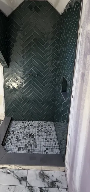 Shower with green glazed tile in a full-height herringbone and a mosaic floor