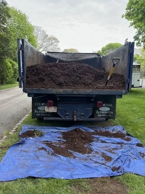 Dump truck unloading dirt onto a blue tarp along a roadside
