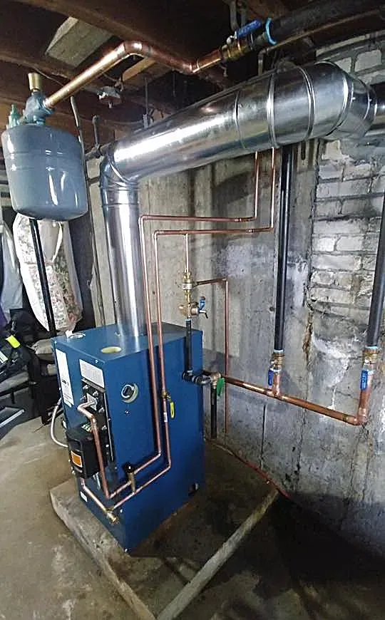 A blue boiler is sitting in a basement next to a brick wall.