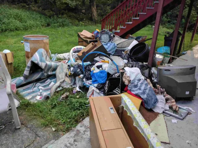 Before junk removal — Household junk in Rehoboth, MA piled up outside a home near a staircase.