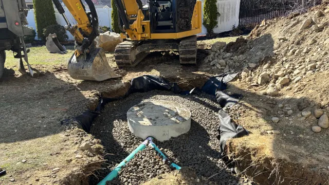 A trench in a yard with a green pipe, gravel, and black fabric for drainage.
