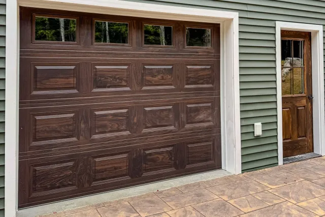 Garage door with windows next to a wooden door on a green siding house.