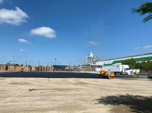 Industrial yard with a blue sky, concrete foreground, parked truck, and distant silos