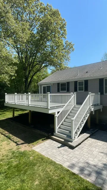House with large white deck and stairs beside a tree on a sunny day
