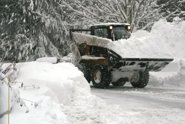 Snowplow clearing a snow-covered road in a winter landscape.