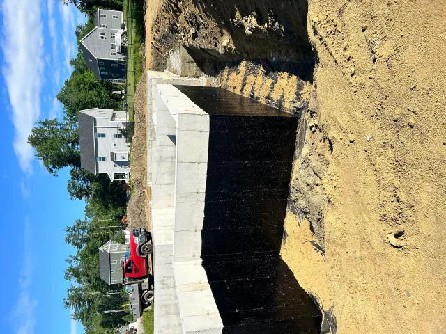 Excavation site with graded earth, concrete foundation, and heavy equipment during residential driveway construction