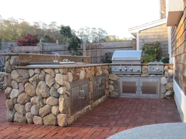 An outdoor kitchen with a grill and a sink made of rocks