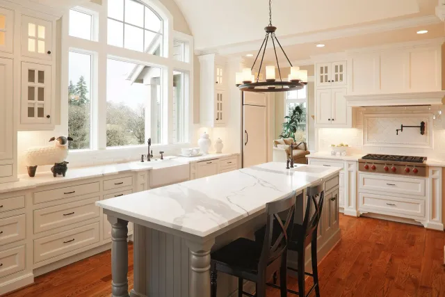 A kitchen with white cabinets , marble counter tops , hardwood floors and a large island.
