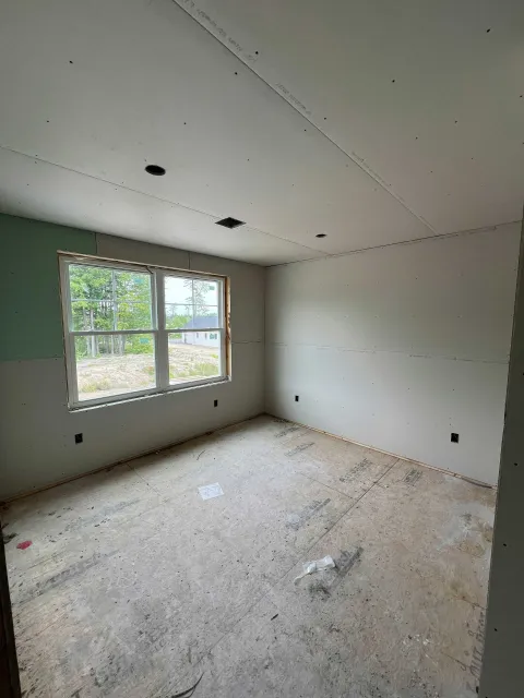 Unfinished room with drywall and a window. Walls are light gray, floor is rough, and the window has an outdoor view.