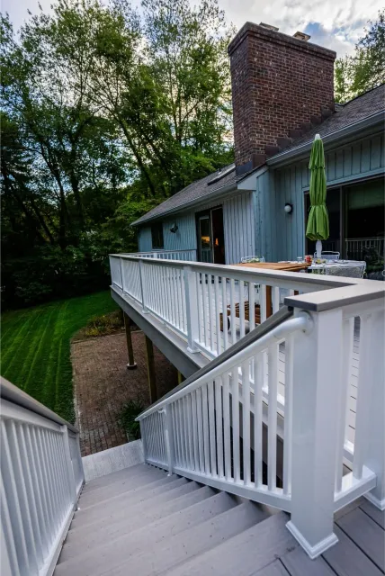 Wooden deck with stairs leading up to a house with a brick chimney and green umbrella.