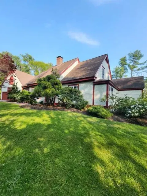 Sunny suburban house with white trim, red roof, and lush green lawn under a blue sky