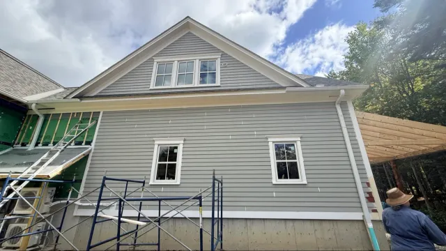 House exterior before repaint: light gray siding, blue sky, scaffolding visible on the side of the house