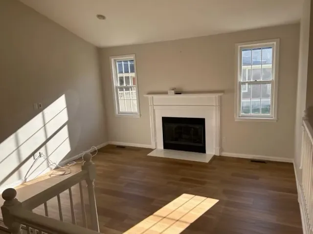 An empty living room with a fireplace and two windows.