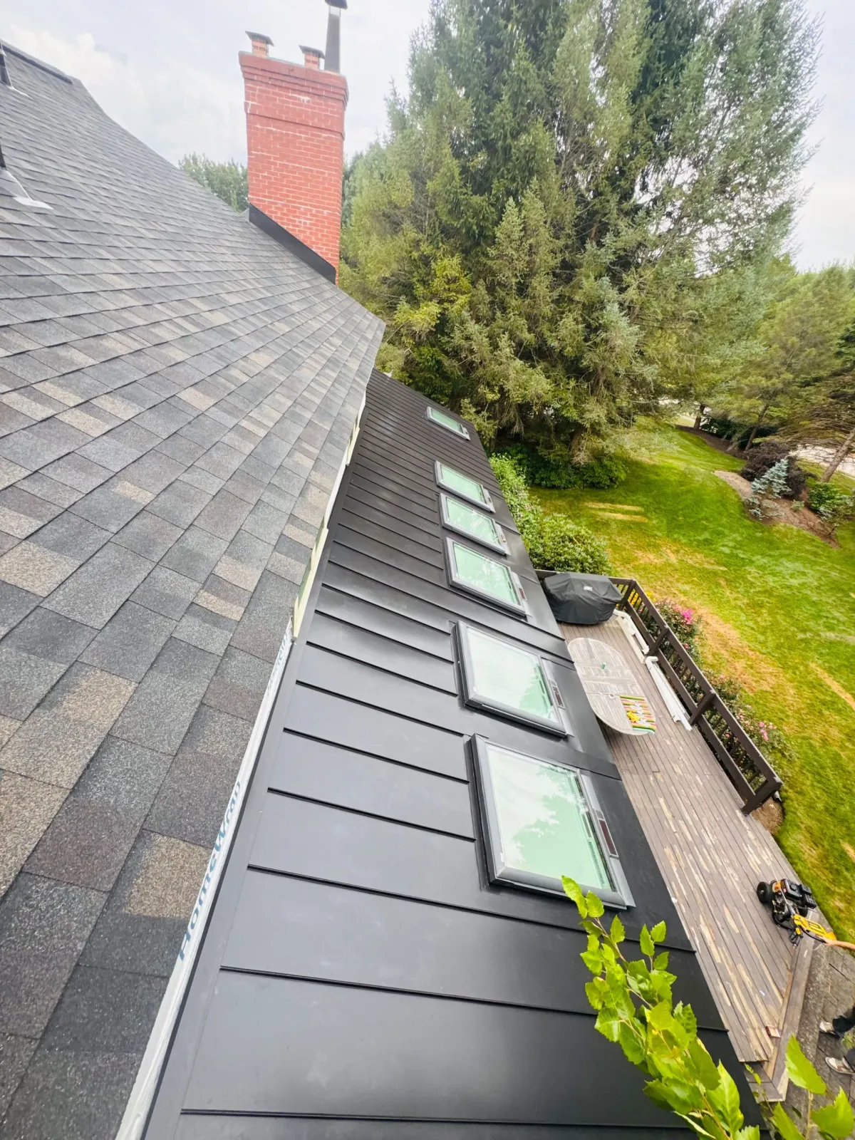 Roof with black skylights beside a brick chimney and green yard.