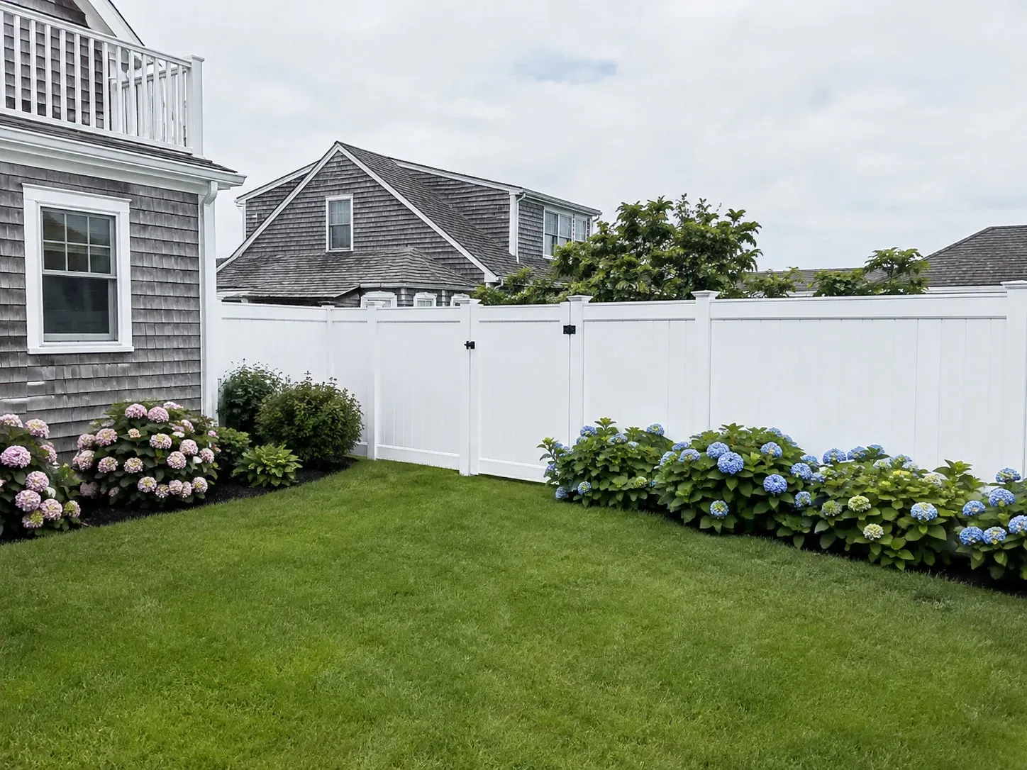 White vinyl privacy fence with a matching gate enclosing a landscaped backyard in Plymouth, MA