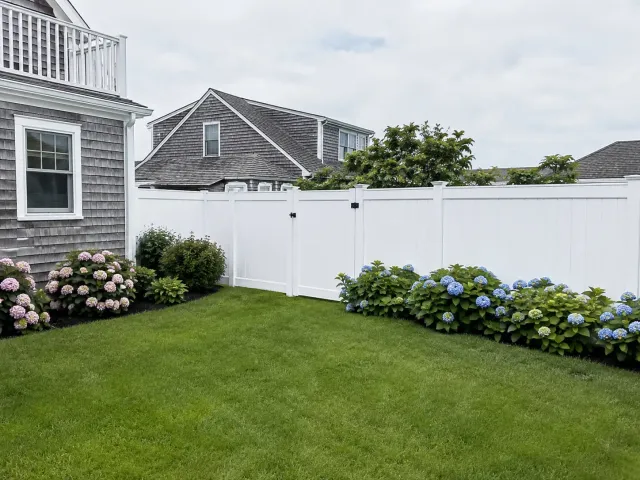 White vinyl privacy fence with a matching gate enclosing a landscaped backyard in Plymouth, MA