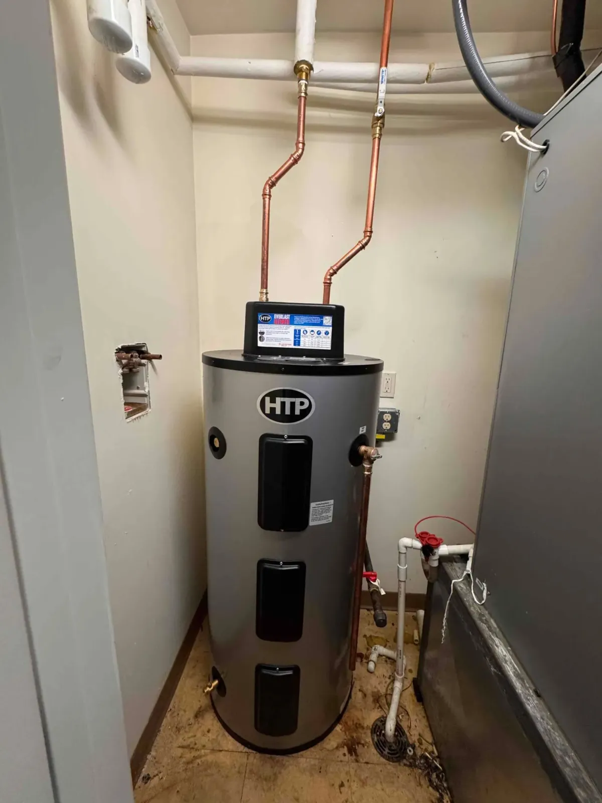 Rheem water heater in a utility closet with copper pipes and a wall-mounted control display