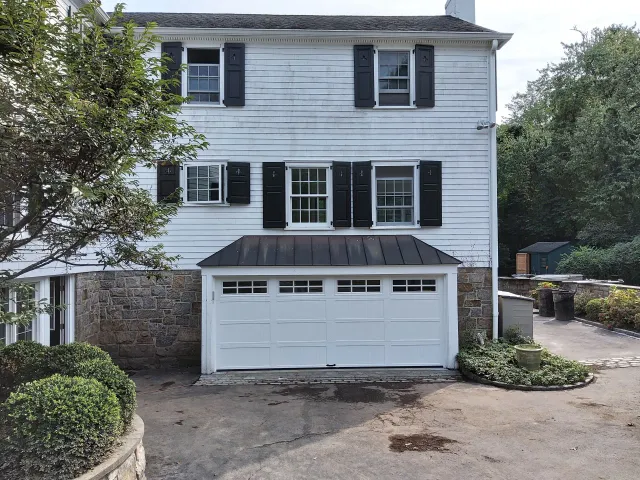 Two-story white house with black shutters and double garage, viewed from the driveway