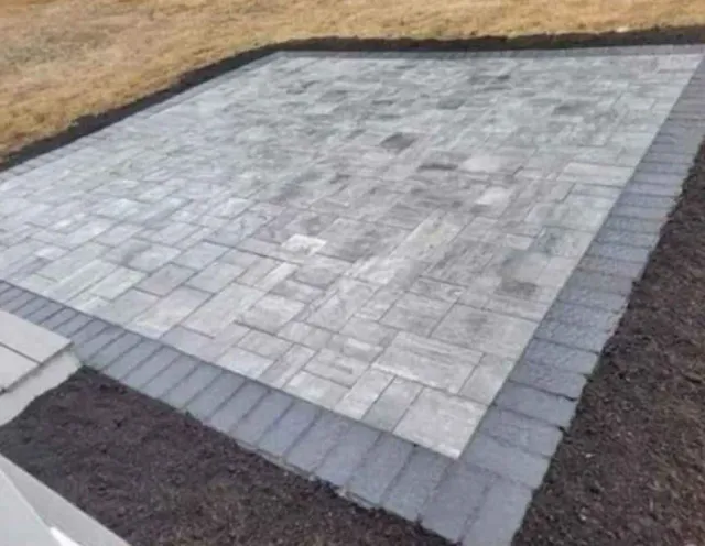 A newly paved gray stone patio bordered by darker edging stones in a yard