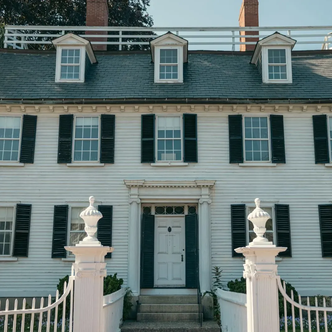White clapboard colonial house with black shutters, dormers and a brick chimney