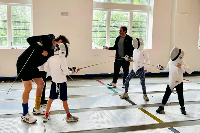 Fencing coaches guide young épée students during a kids’ class at Allez Fencing Club in Watertown, MA, focusing on technique, positioning, and confidence building.