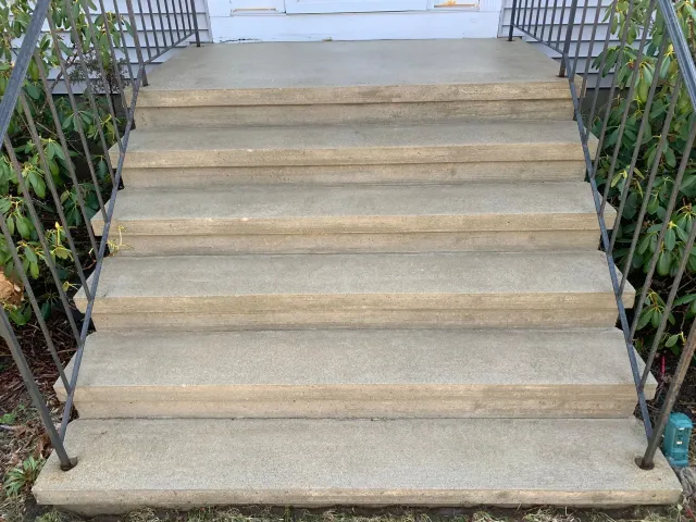 A set of concrete stairs leading up to a house with a metal railing.