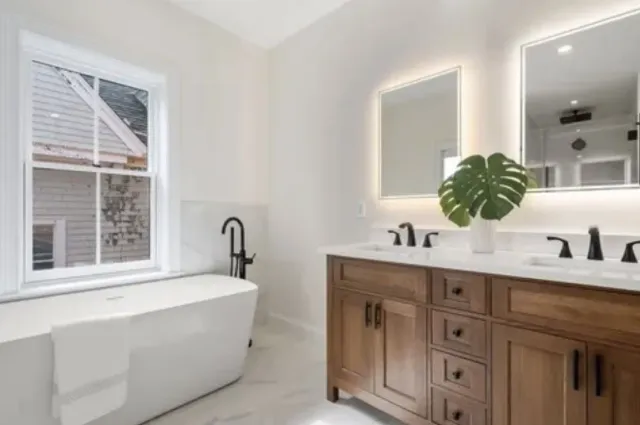 A bathroom with a tub, sinks, mirrors, and a window.