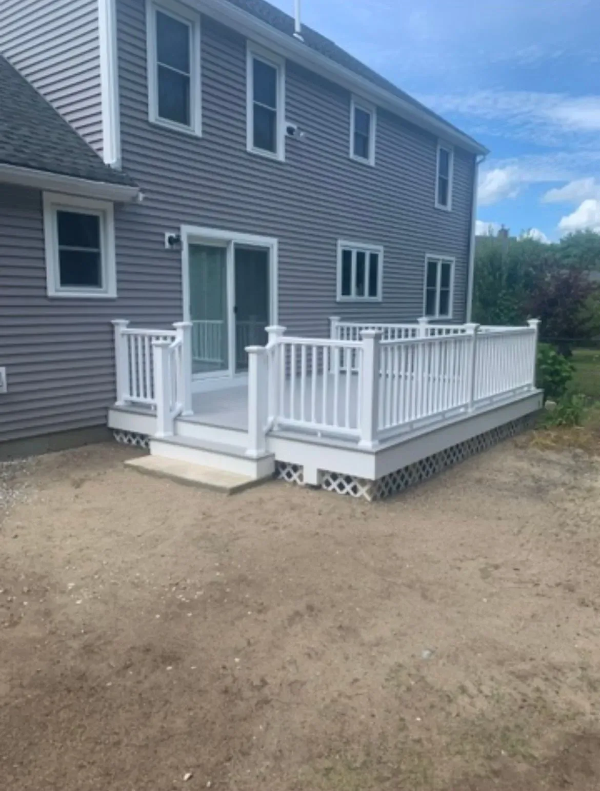 Backyard deck with white railing and steps beside a gray house on a gravel yard